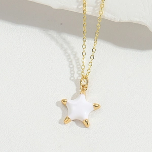 Detailed close-up of a gold-plated star pendant with white enamel on a thin chain