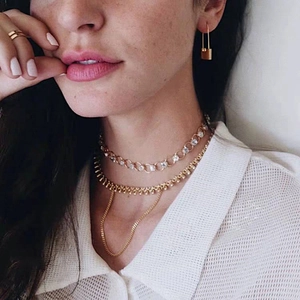 Close-up of golden lock earrings and layered necklaces on a model with minimalist style