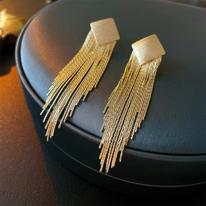 Detailed close-up of golden fringe tassel earrings on a navy blue jewelry box