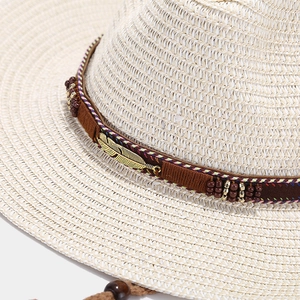 Detail of straw cowboy hat featuring metallic feather and bohemian embroidered band