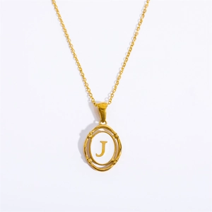 Macro detail of gold oval pendant featuring a white background and gold letter J charm
