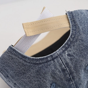 Macro detail of denim baseball cap showing the adjustable velcro strap and premium stitching