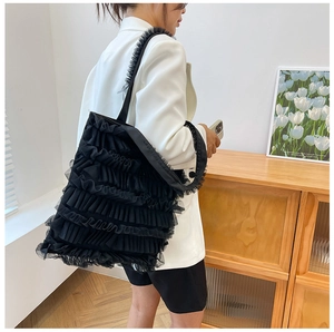 Side view of a black ruffled lace tote bag carried by a model in a stylish indoor setting.