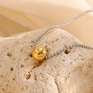 Close-up of a minimalist 18K gold bead pendant on a silver ball chain over stone