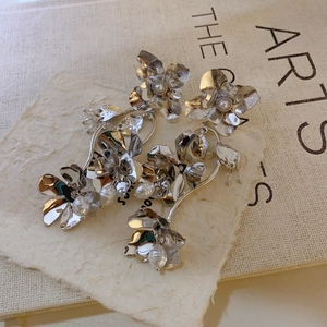 Detail of silver floral earrings featuring baroque pearls and textured petals on a vintage background