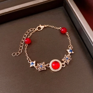 Detail view of rose gold bracelet with red beads and blue stars in a brown gift box