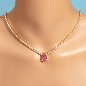 Close-up of golden necklace featuring a pink teardrop zircon on a model's neck