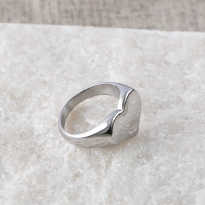Polished silver heart signet ring in stainless steel displayed on white marble stone
