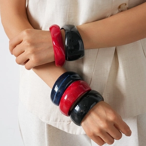 Irregular acrylic resin bangle bracelets in red, blue, and black shown on a model