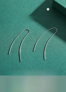 Detail of minimalist S925 sterling silver U-shaped threader earrings on dark green background