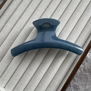 Close-up of a 11cm curved navy blue claw clip on a soft beige velvet jewelry display