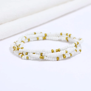 Detail of four-layered elastic beaded bracelet with white and gold seed beads on fabric