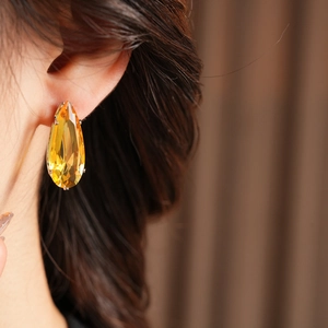 Macro view of bright yellow teardrop cut earrings with silver needle on ear