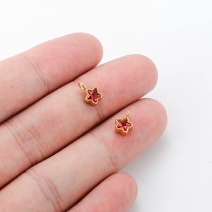 Handheld view of two mini gold stainless steel star charms with pink zircon inlay