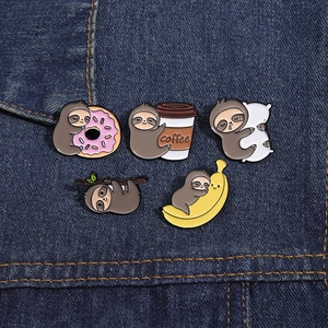 Detailed view of five cute enamel sloth pins with sweets and coffee on denim fabric