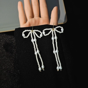 Close-up of pearl bow tassel earrings with white pearls on a black background