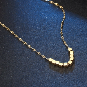 Elegant gold titanium steel necklace with square bead pendants on a textured blue background