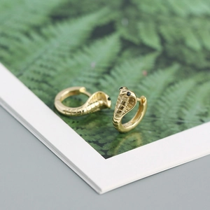 Detailed macro view of gold cobra snake hoop earrings with black gemstone eyes