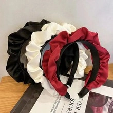 Close-up of pleated satin headbands in black, white and burgundy on a wooden table