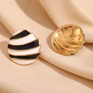 Macro view of gold-plated oval stud earrings featuring black and white striped enamel details