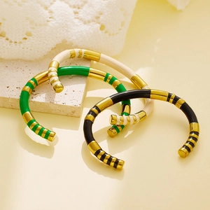 Three gold-plated enamel bangles in green, black, and white on a stone display stand