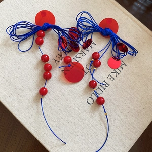 Detail of handcrafted geometric earrings with blue rope, red beads, and sequins