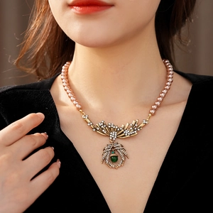 Close-up of vintage pink pearl necklace featuring leaf pendant with green gemstone