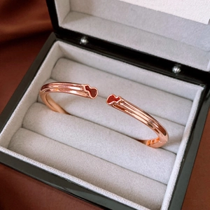 Détail du bracelet ouvert en or rose avec gourdes en émail rouge dans un coffret cadeau