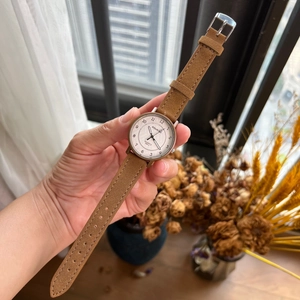 Close-up of a white dial quartz watch with a brown suede leather strap and silver case
