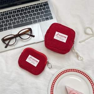 Detail of red corduroy coin purses with brand labels next to a laptop and accessories