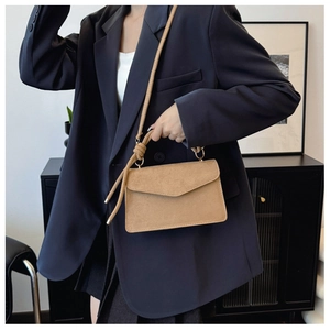 Detail of camel suede handbag featuring knot shoulder strap and elegant top handle on model