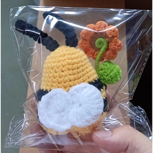 Detail of a handmade crochet bee plush with orange flower in transparent packaging