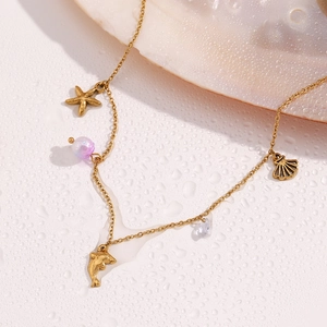 Detailed macro shot of 18K gold plated starfish and shell ocean charms on a gold chain