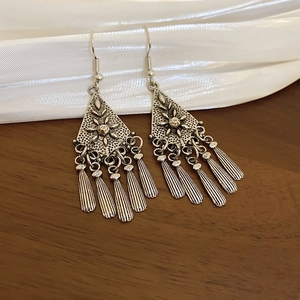 Detail of silver bamboo flower earrings with pearl tassels on white silk and dark wood