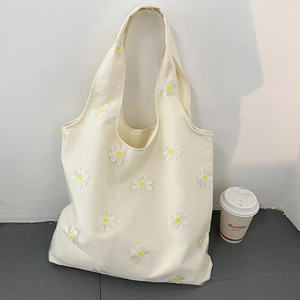 Off-white canvas tote bag featuring delicate daisy embroidery and wide shoulder straps