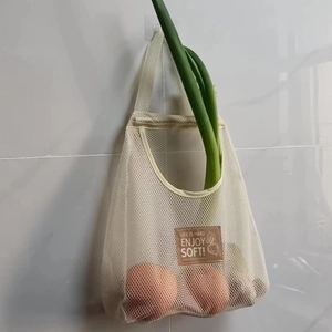Detail of breathable cream mesh storage bag holding onions on a white tiled wall