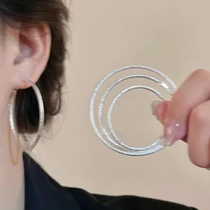 Detailed view of silver hoop earrings with a frosted finish shown on a model