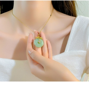 Close-up of a gold necklace featuring a translucent green round pendant with leaf detail