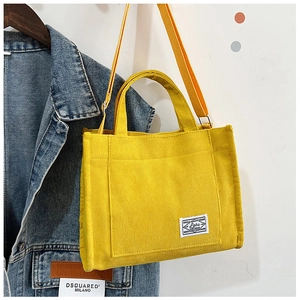 Detail of yellow corduroy tote bag with woven label hanging on a denim jacket