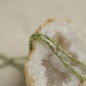 Macro shot of olive green faceted beads draped over a white crystal cluster gemstone