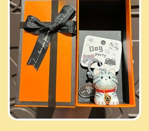 Cute grey striped cat keychain with a red collar and golden bell in an orange gift box