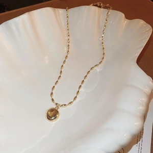 Detailed close-up of a gold necklace with a round cat-eye stone pendant in a white shell dish