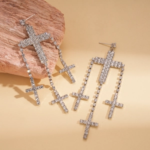 Detailed close-up of silver tassel cross earrings with white rhinestones on rock props
