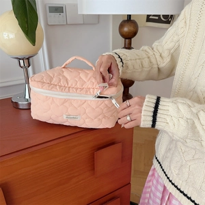 Dettaglio della borsa da toilette trapuntata a cuore con cerniera e sfondo in legno