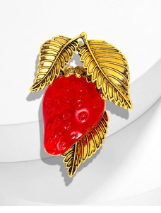 Detail of red strawberry enamel brooch with gold textured leaves on white stand
