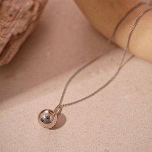 Gros plan d'un pendentif boule en acier inoxydable argenté et chaîne fine sur pierre