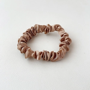 Detailed view of champagne satin scrunchie with smooth silk texture and elegant pleats