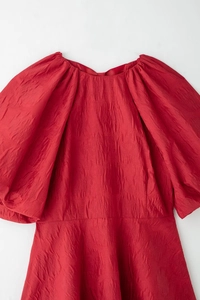Détail du tissu rouge texturé avec manches bouffantes et une encolure ronde élégante