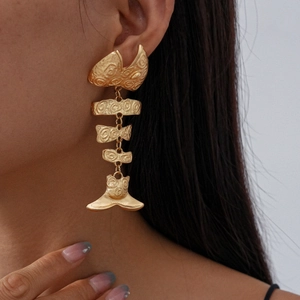 Close-up of long gold fishbone pendant earrings with spiral texture on a model
