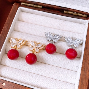 Detail view of butterfly drop earrings with red pearls and zircon in a jewelry box